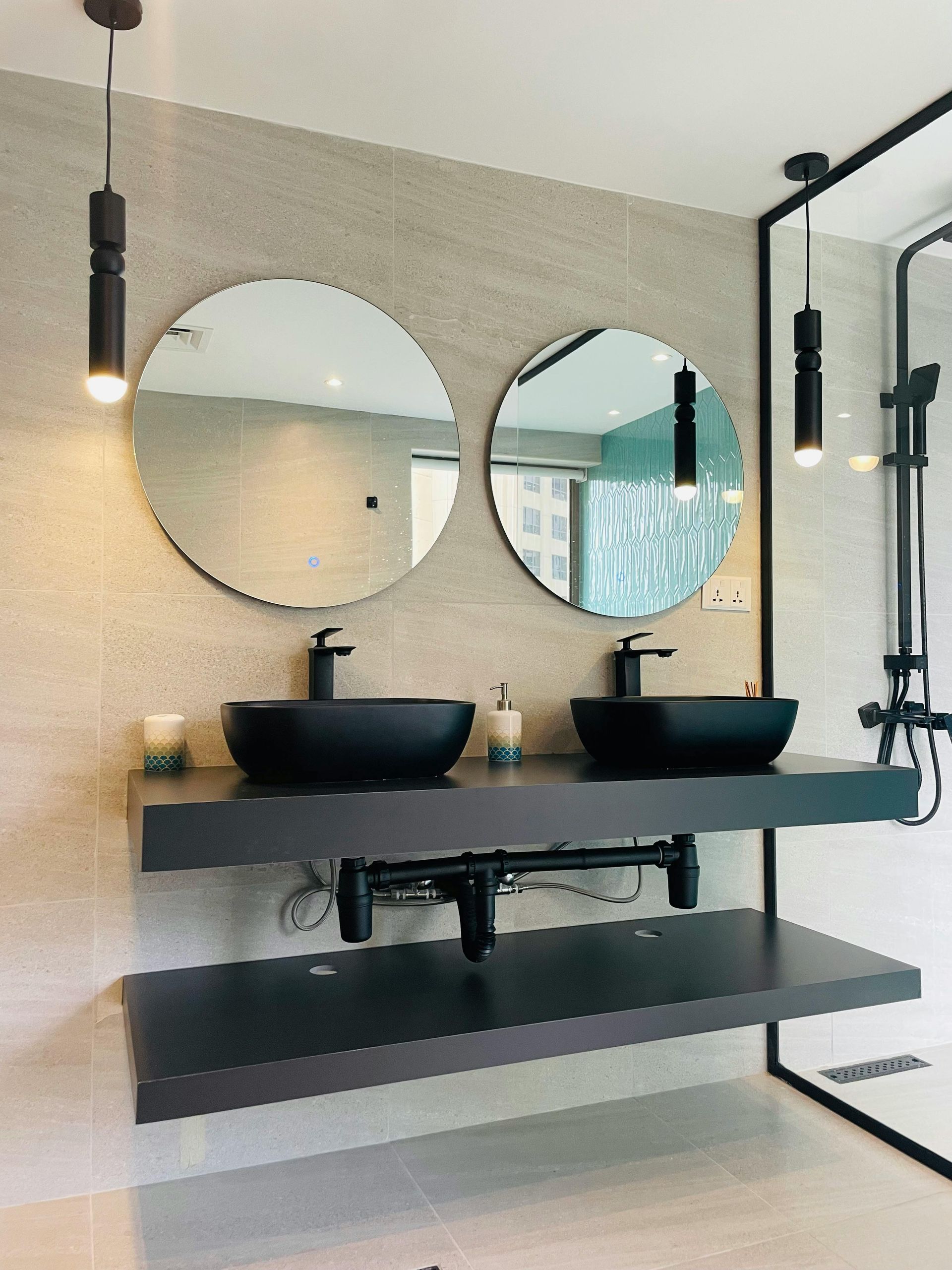 Modern bathroom with black sinks, round mirrors, and black fixtures against a neutral tiled wall.