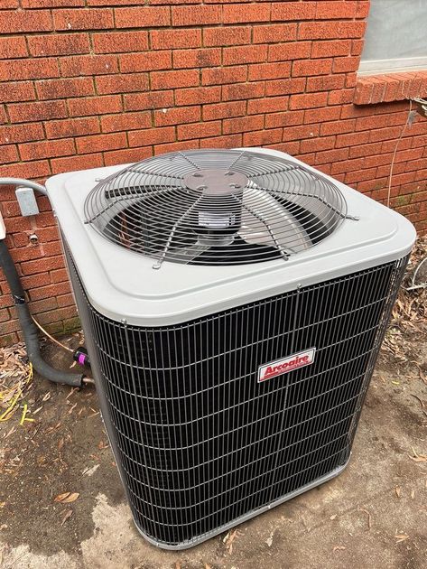 A large air conditioner is sitting in front of a brick building.