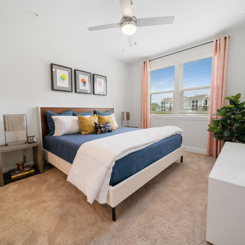Bedroom with a bed, nightstand, dresser, and wall art; neutral colors with blue and yellow accents.