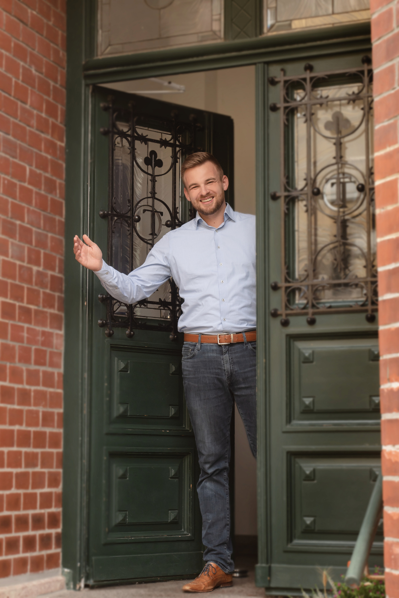 Ein Mann steht vor einer grünen Tür und winkt.