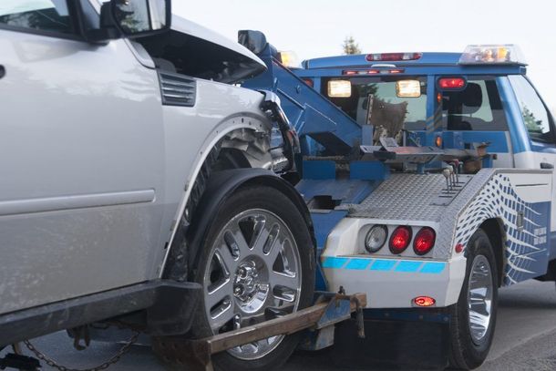 A silver car is being towed by a blue tow truck.