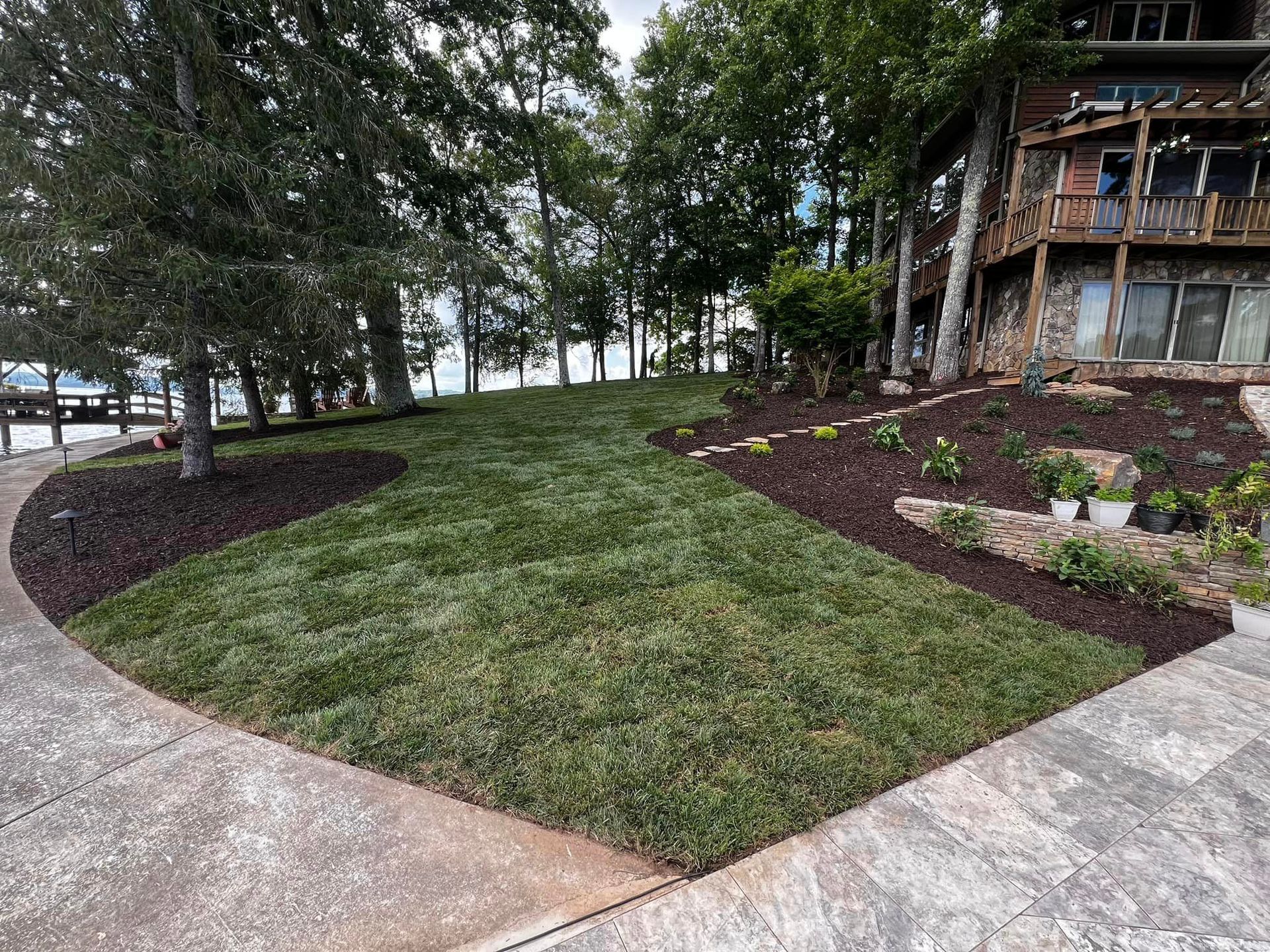 A lush green lawn is surrounded by trees and bushes in front of a house.