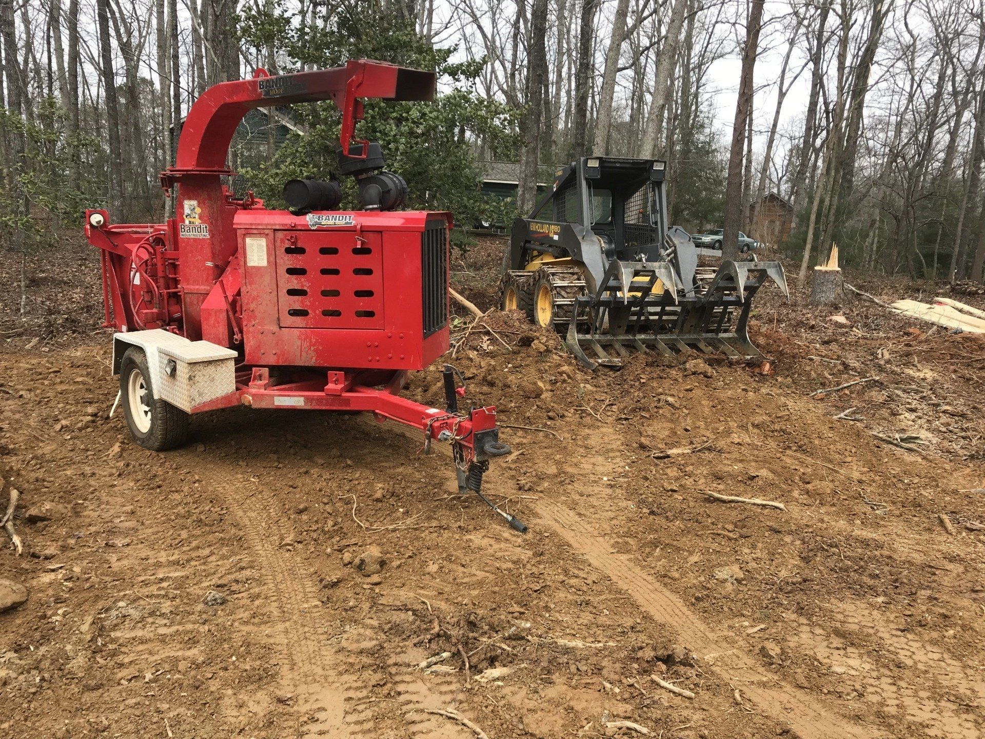 A red chipper is parked on a dirt road next to a bulldozer.
