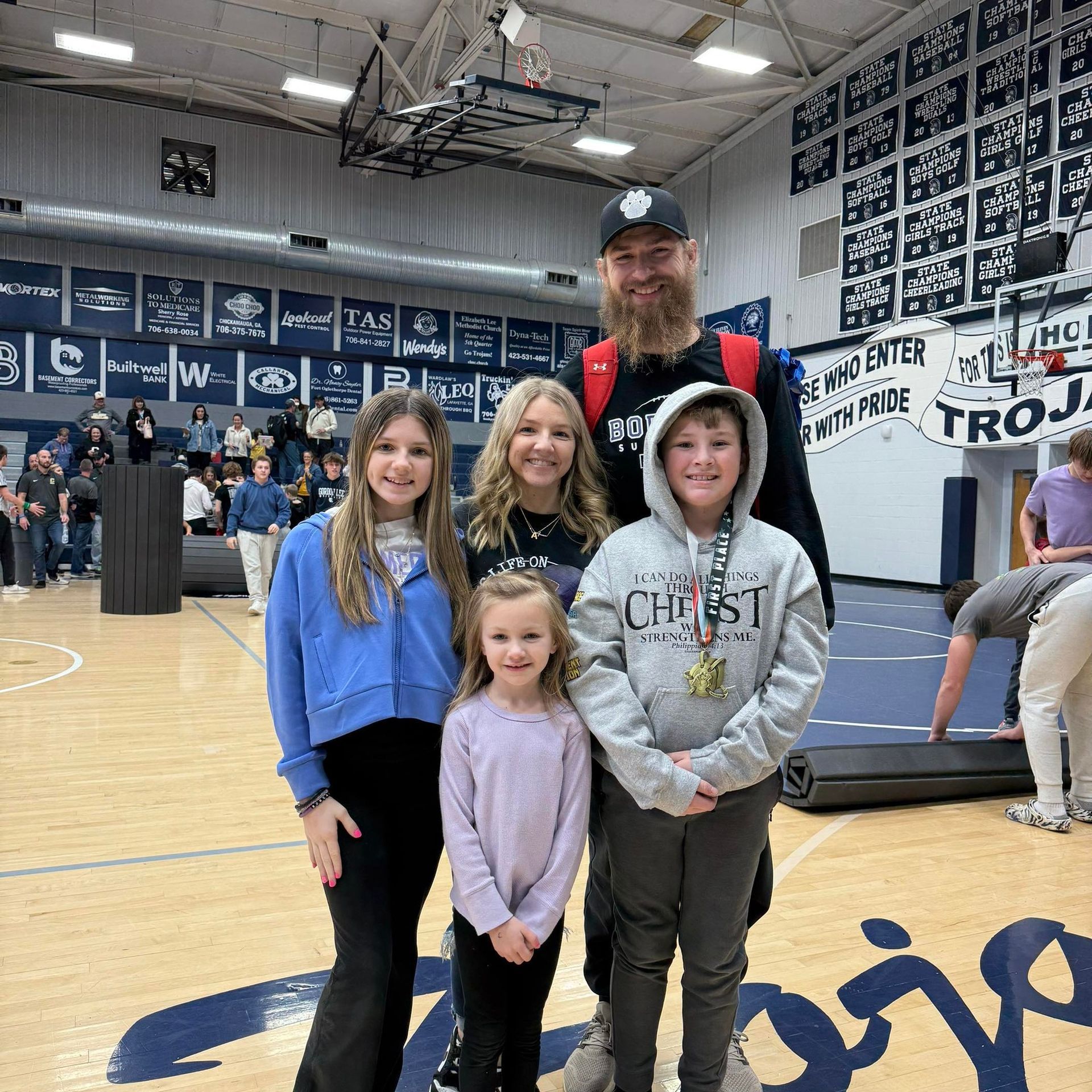 A family posing for a picture on a basketball court in front of a wall that says trojans