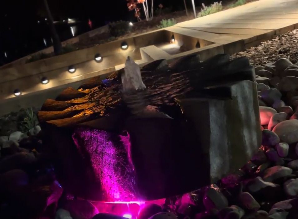 a water fountain is lit up with pink lights at night