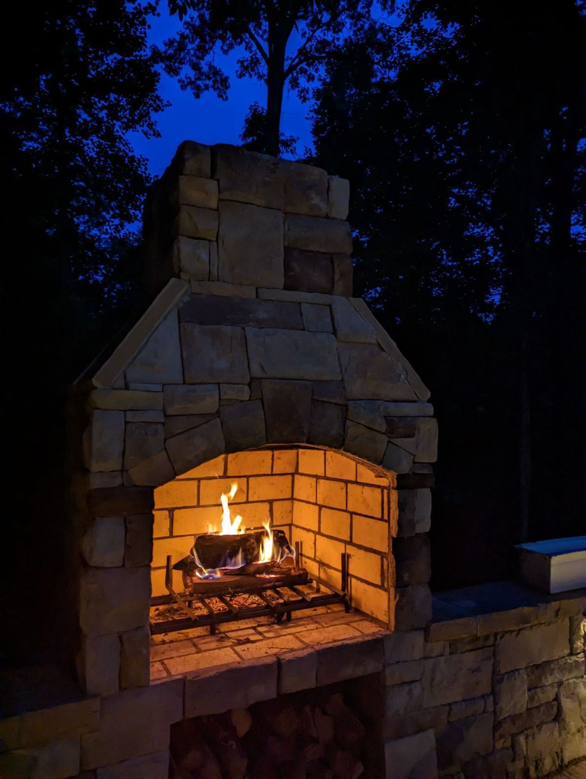 A fireplace is lit up at night with trees in the background
