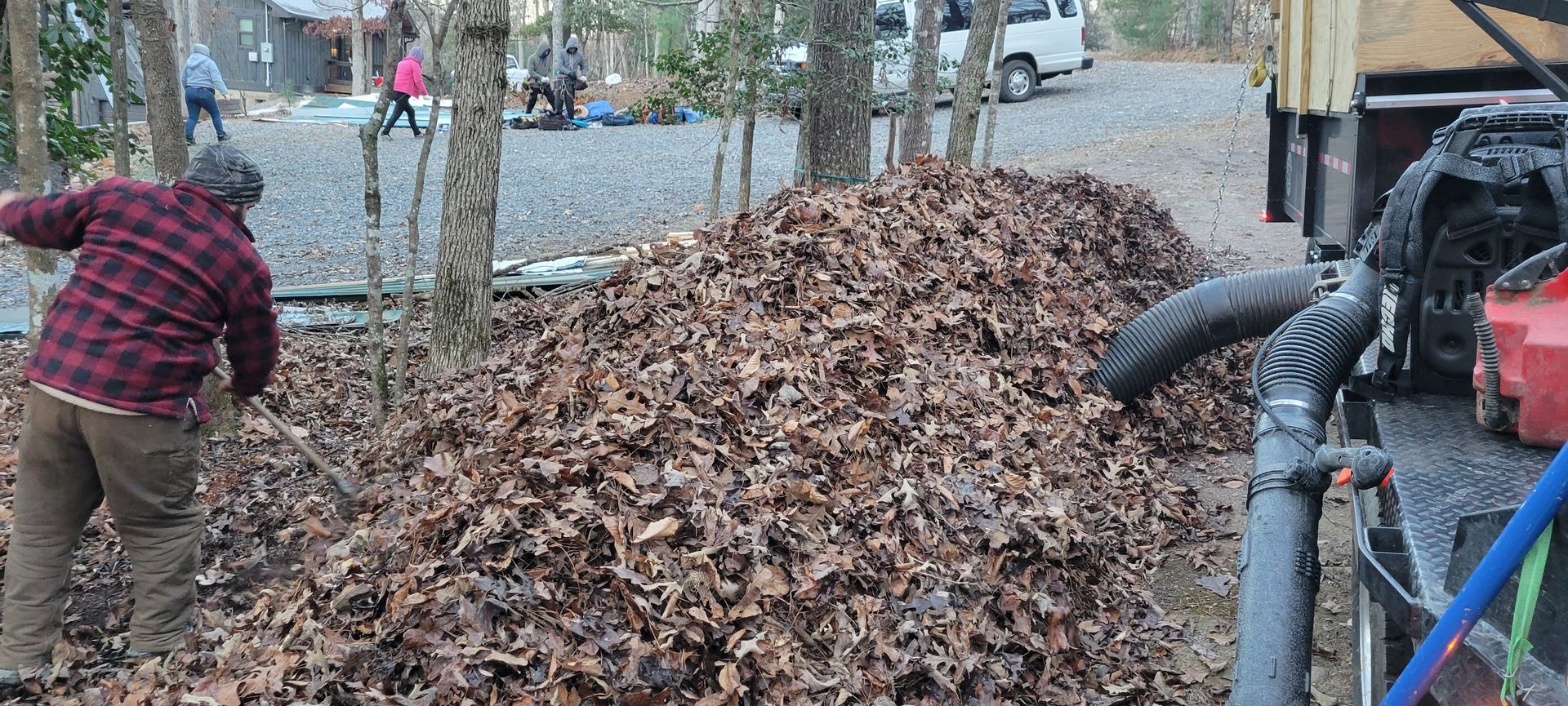 A man in a plaid shirt is standing next to a pile of leaves