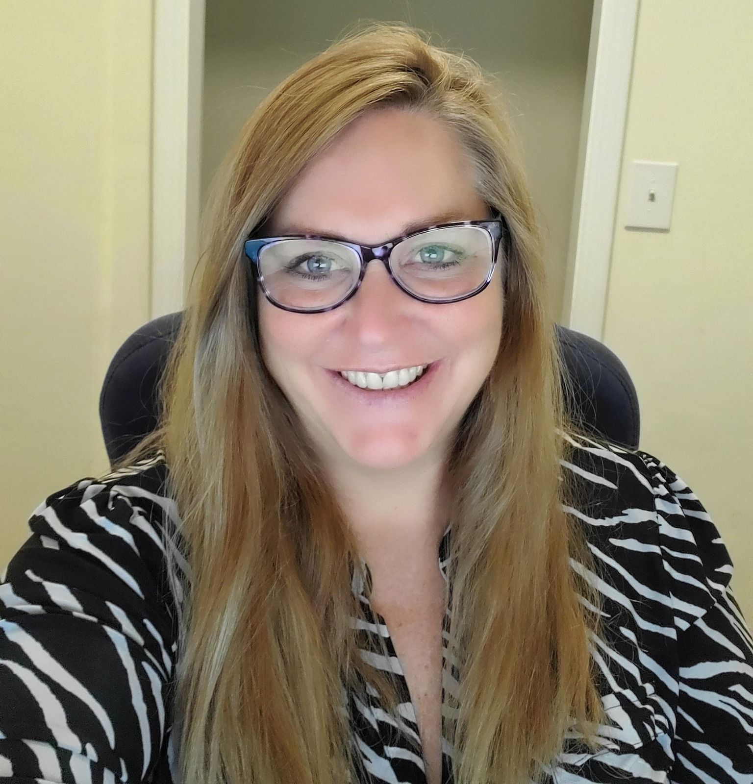 A woman wearing glasses and a zebra print shirt smiles for the camera