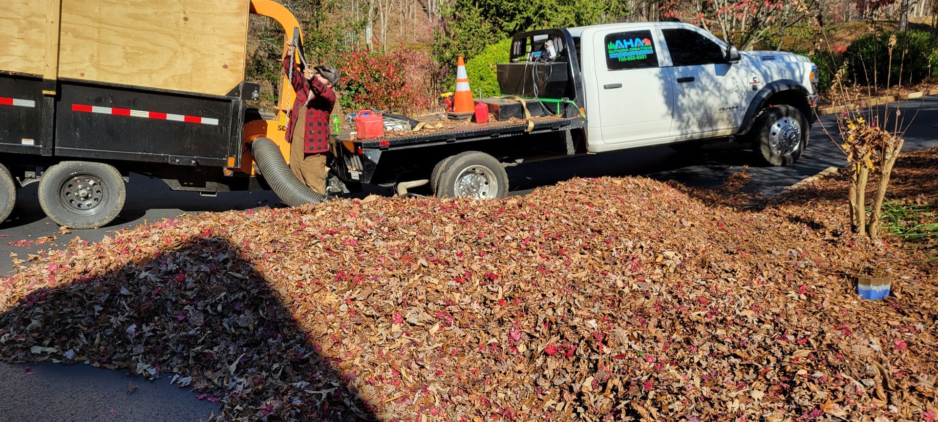 A white truck and trailer with a wood chipper processing wood chips onto a large pile on a driveway.