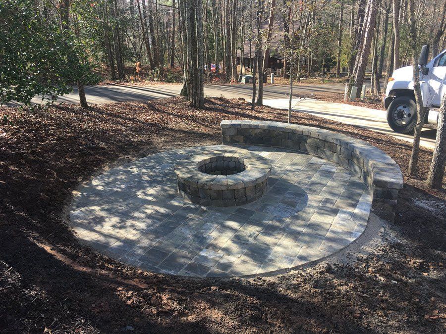 A fire pit is surrounded by a brick patio and trees