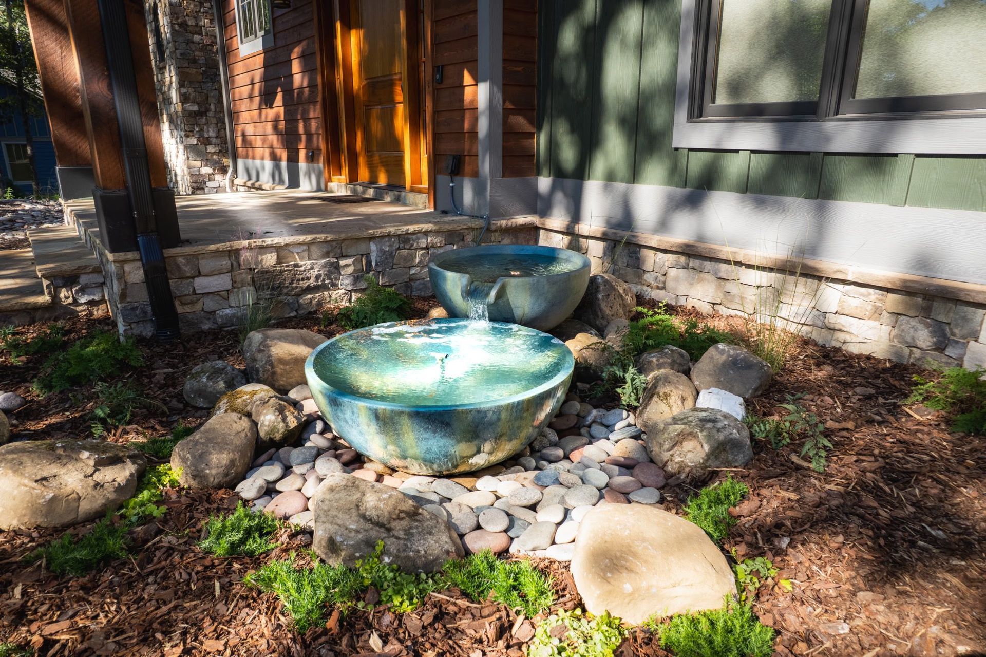 Water fountain with blue glazed bowls, surrounded by rocks and plants.