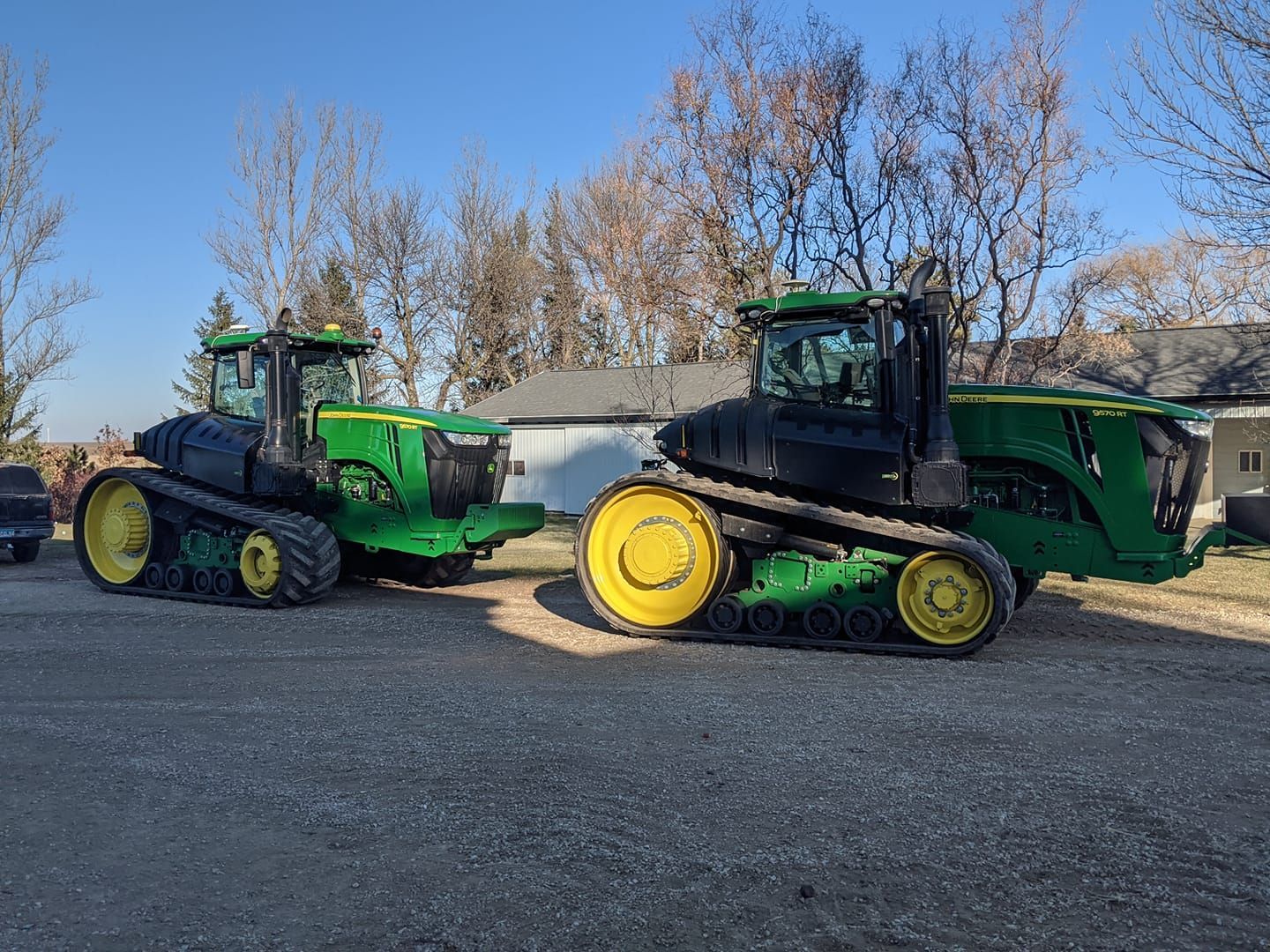 Two john deere tractors are parked next to each other on a gravel road.