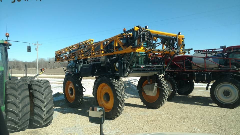 A row of tractors are parked in a gravel lot.