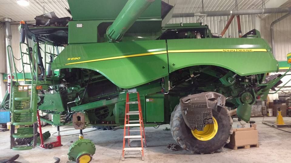 A green john deere combine harvester is being repaired in a garage.