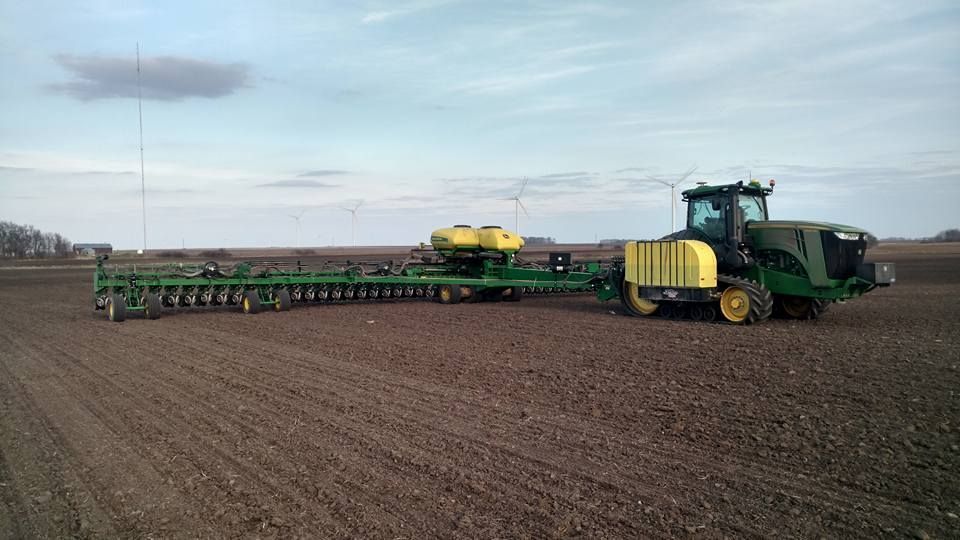 A john deere tractor is plowing a field with a planter attached to it.
