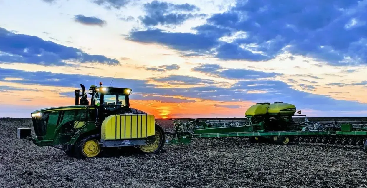 A john deere tractor is plowing a field at sunset