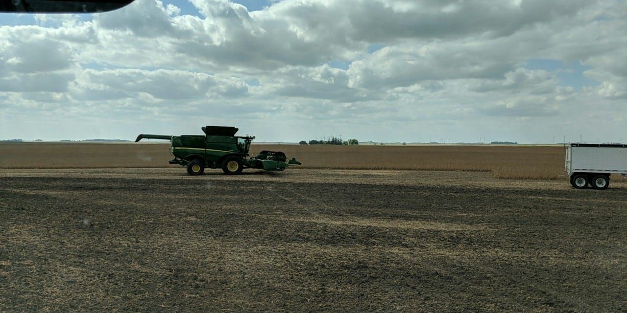 A combine harvester is driving down a dirt road next to a trailer.