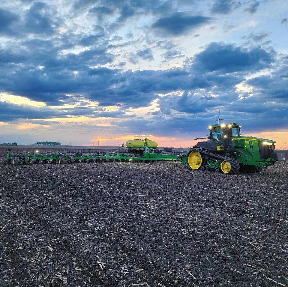 A john deere tractor is plowing a field at sunset