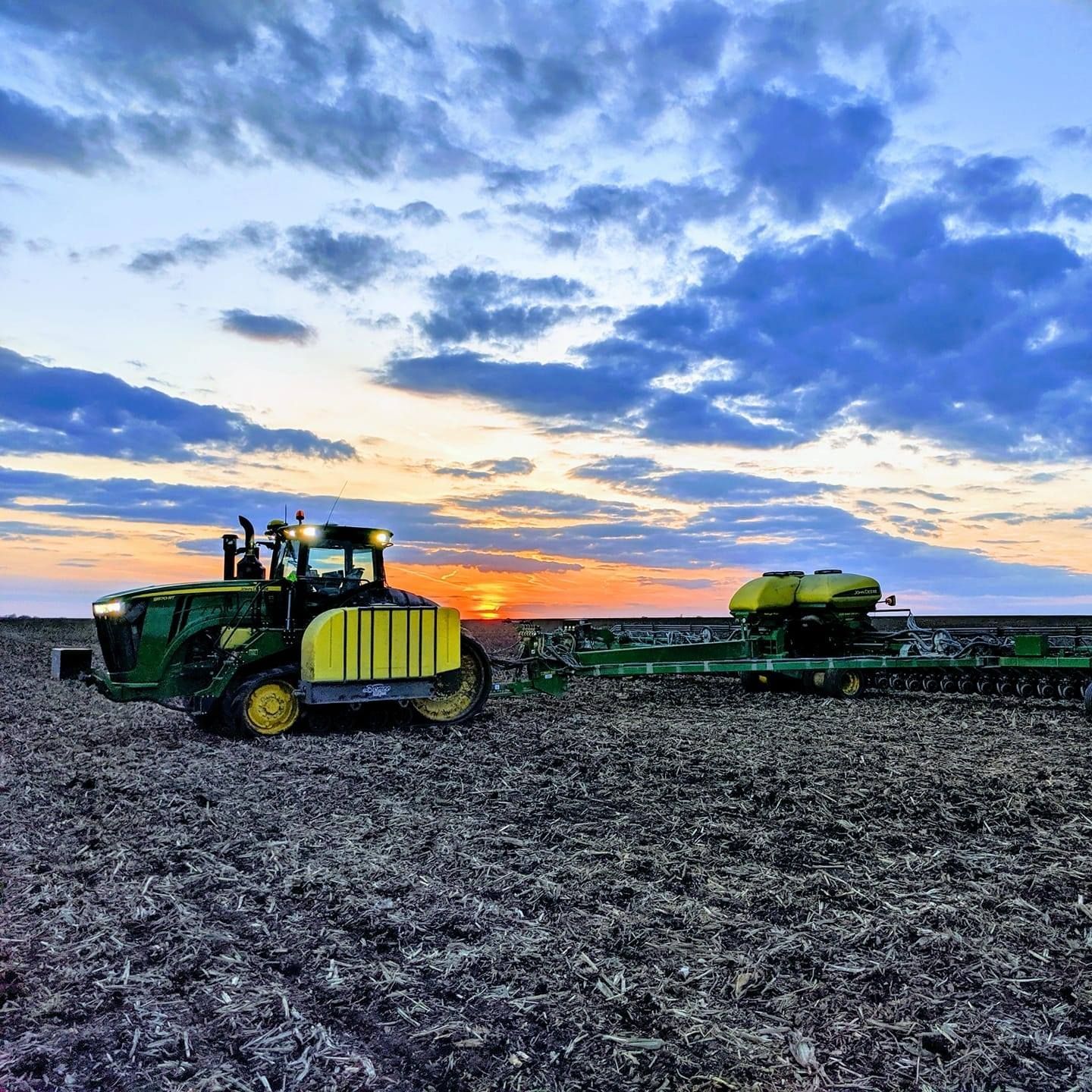 A john deere tractor is plowing a field at sunset