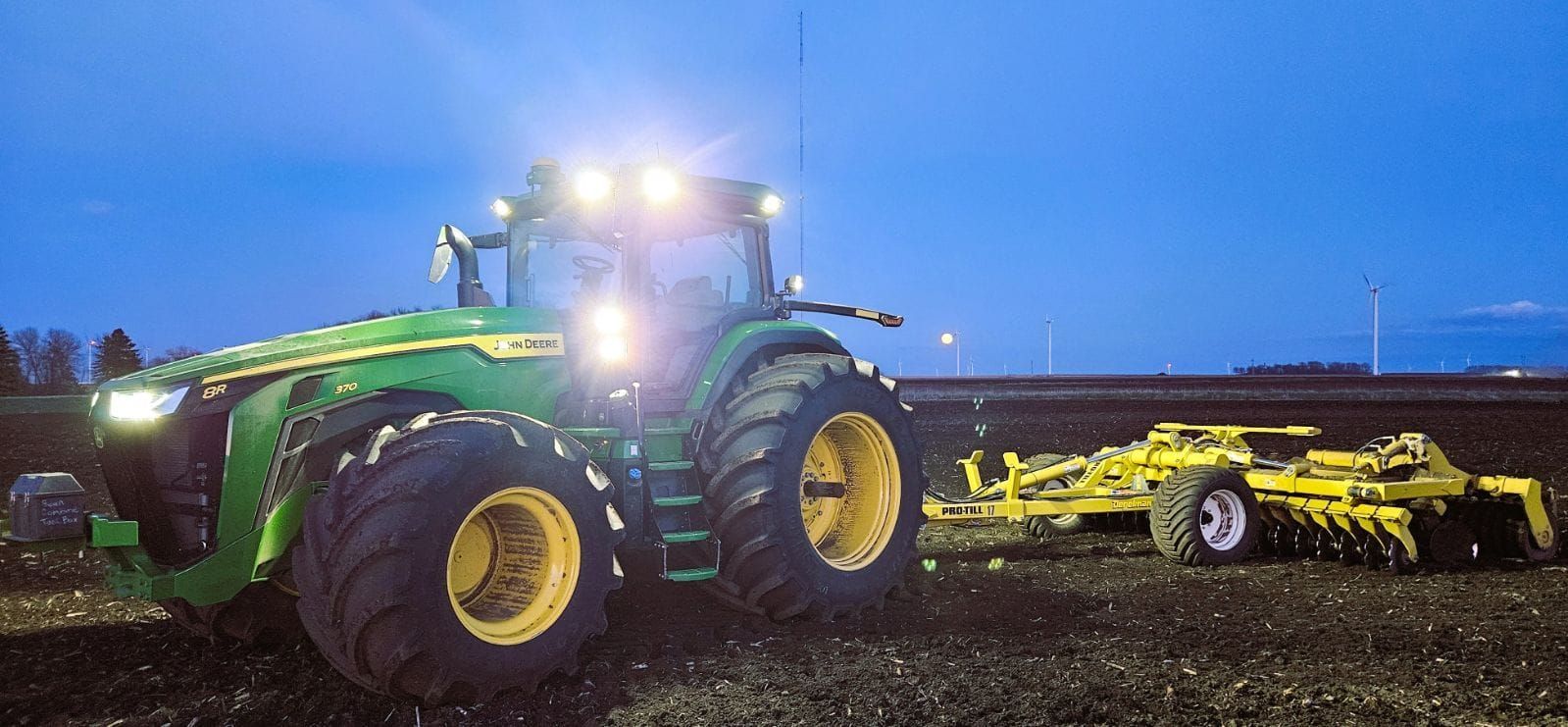 A john deere tractor is driving through a field at night