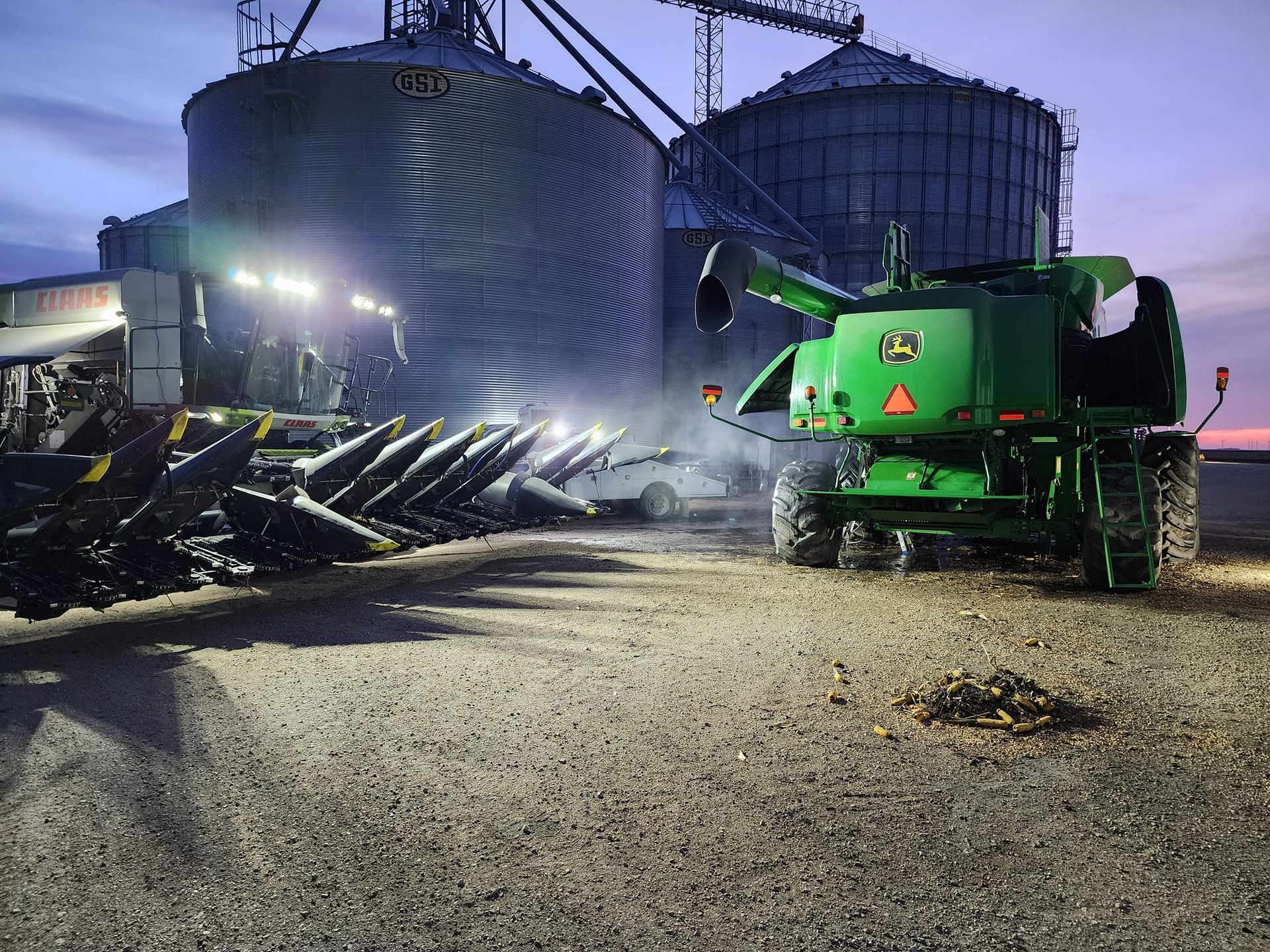 A green tractor is parked in front of a grain silo at night.