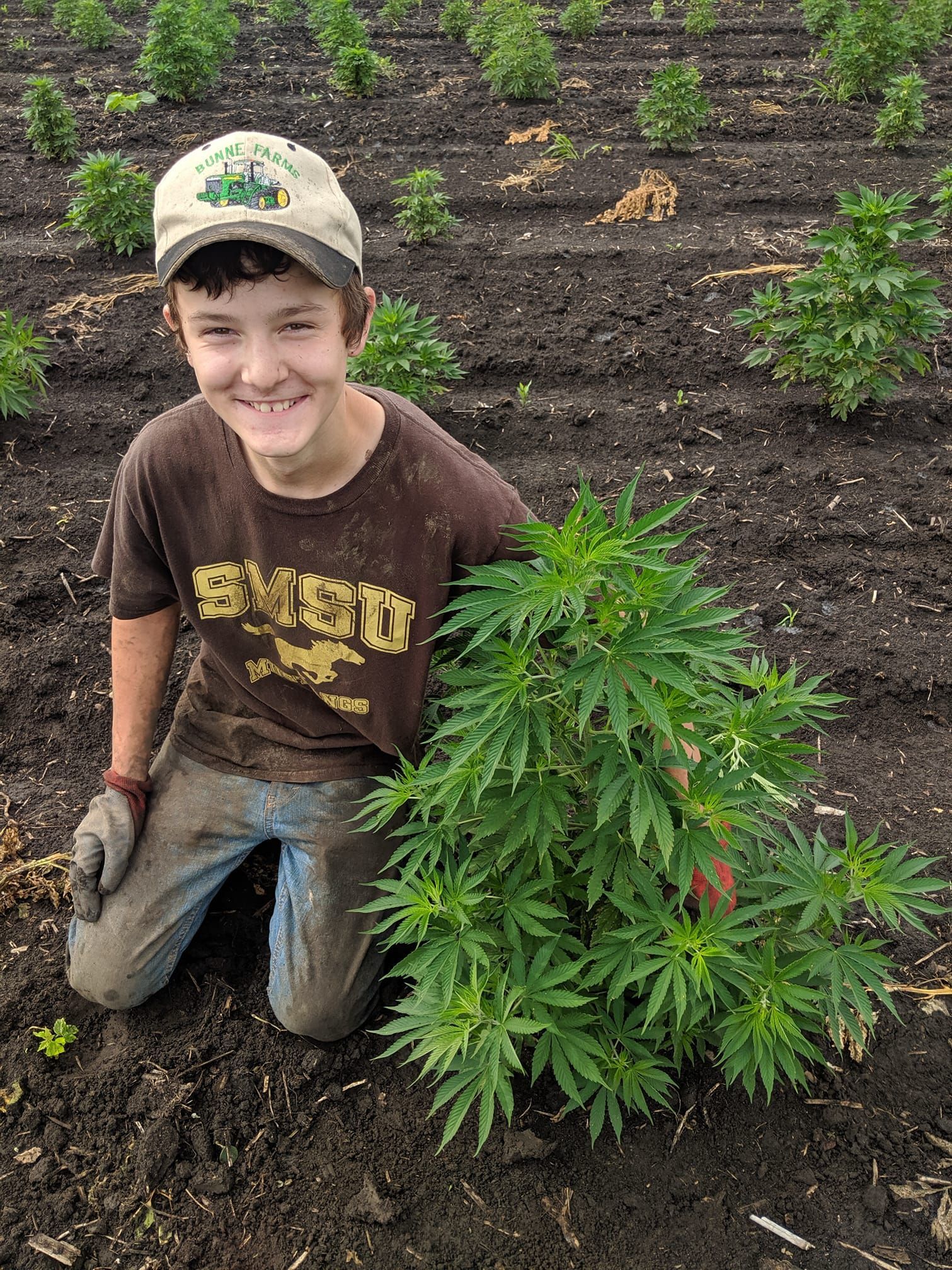 A boy smiling with a plant beside him