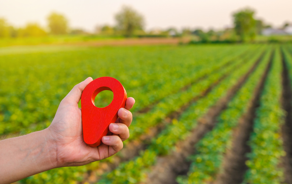 A person is holding a red pin in front of a field.