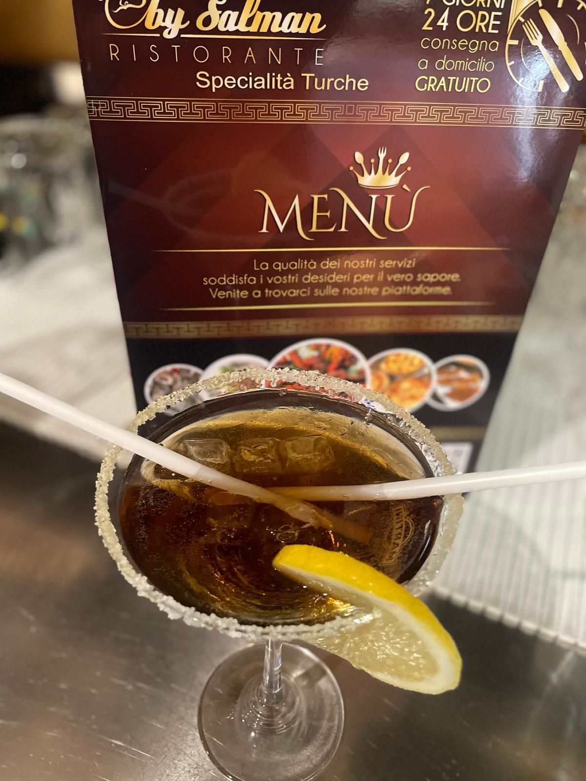 Un bicchiere con il bordo zuccherato, un drink con ghiaccio e una fetta di limone e il menù di un ristorante.