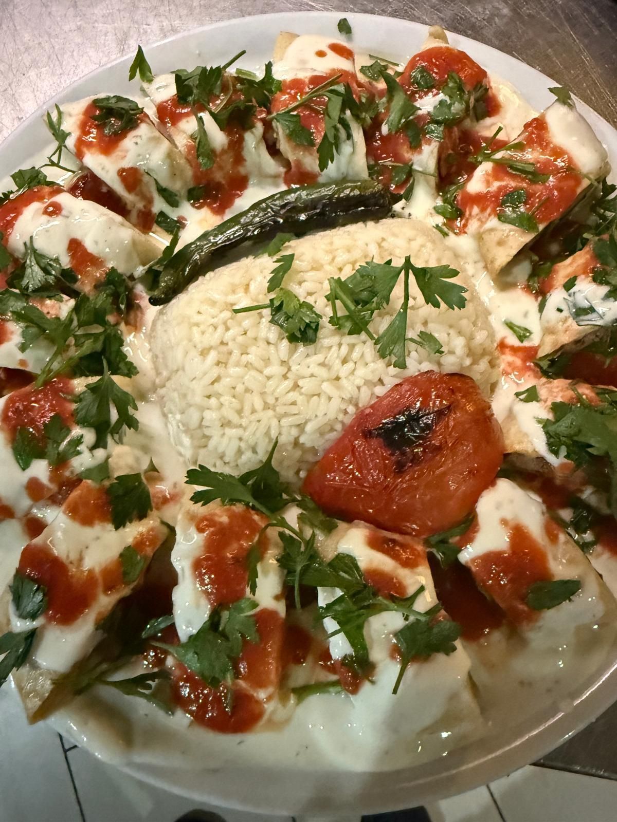 Piatto di ravioli turchi manti con salsa allo yogurt, salsa di pomodoro, riso, pomodori arrostiti e prezzemolo.