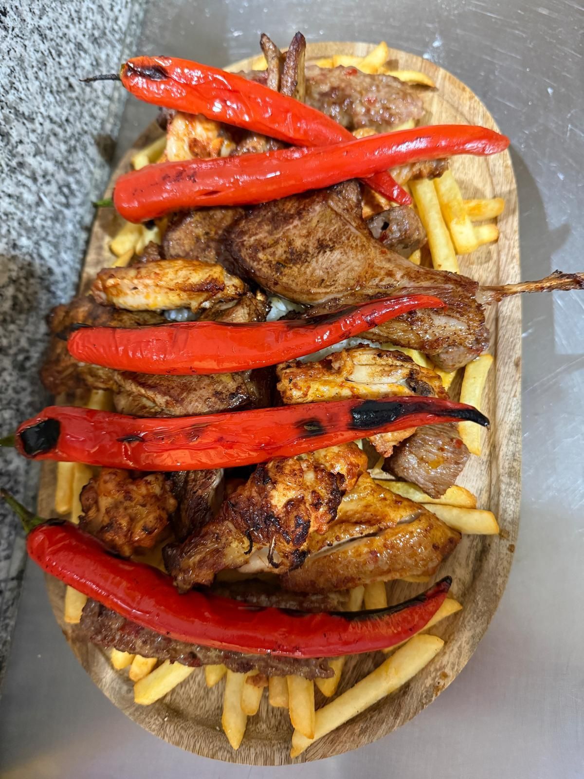 Piatto di carne alla griglia con patatine fritte e peperoni rossi su un tagliere di legno.