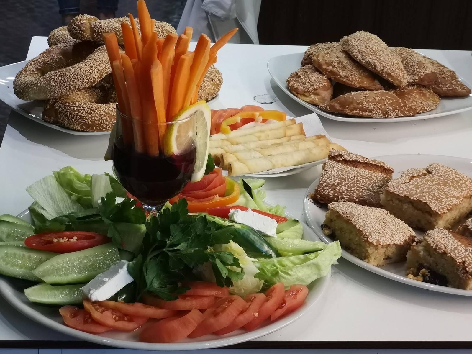 Assortimento di cibi turchi per la colazione su piatti bianchi: insalata, bagel simit, bastoncini di carota, pasticcini.