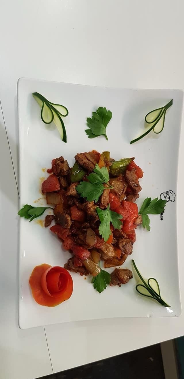 Un piatto di cibo guarnito con coriandolo e cetriolo. A lato, una decorazione a forma di rosa di pomodoro.