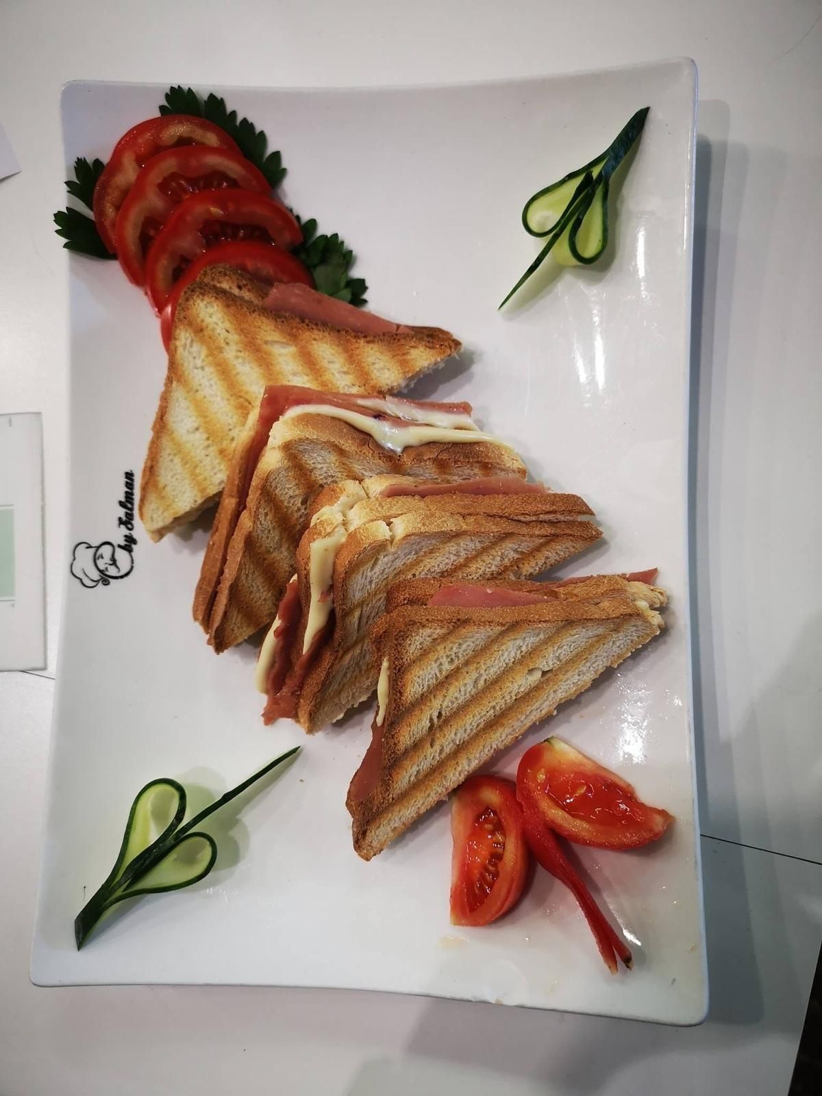 Panini grigliati su un piatto bianco, serviti con fette di pomodoro e guarnizioni di cetriolo.