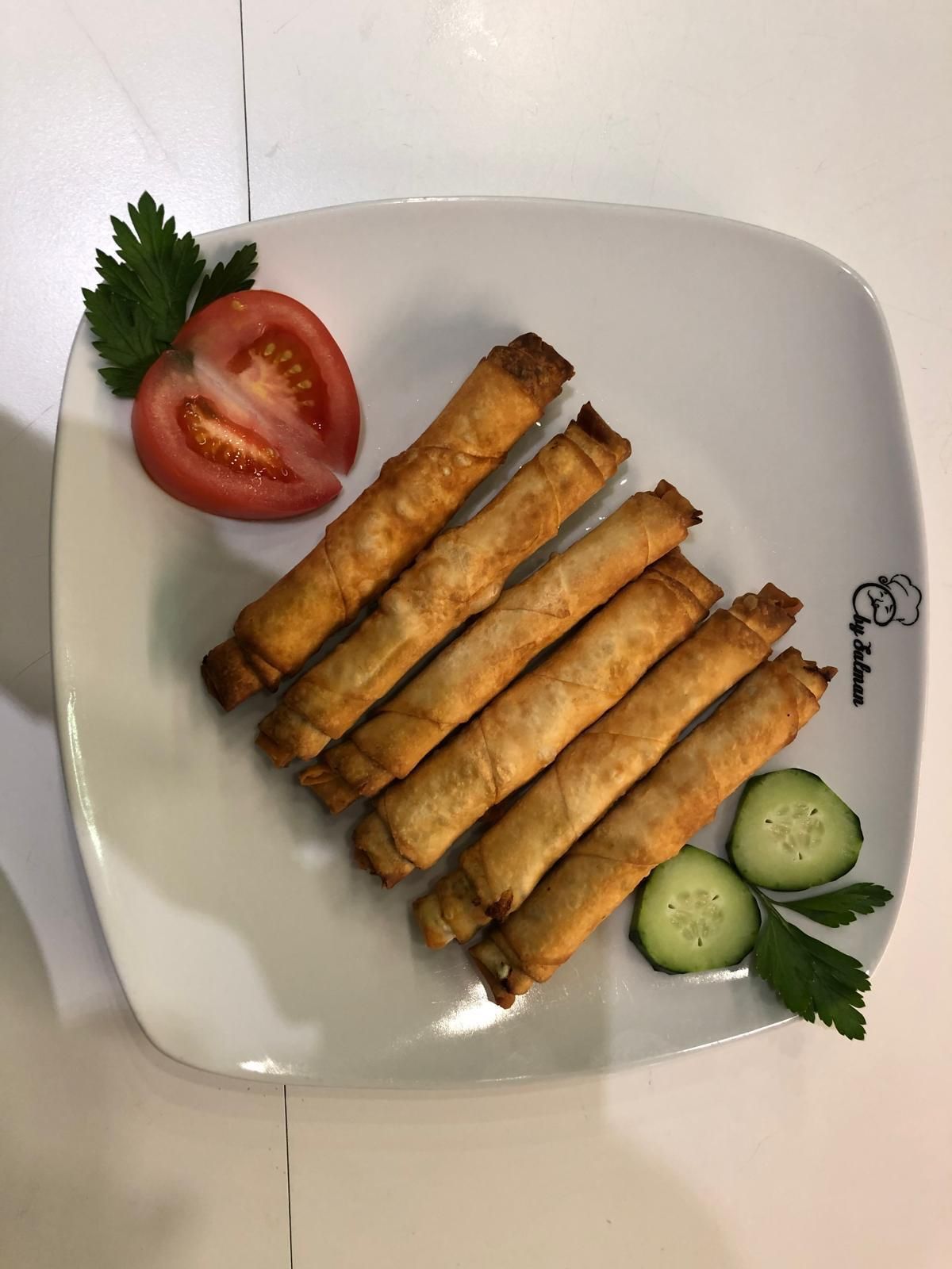 Piatto di rotoli di pasta fritti, fette di pomodoro e cetriolo.