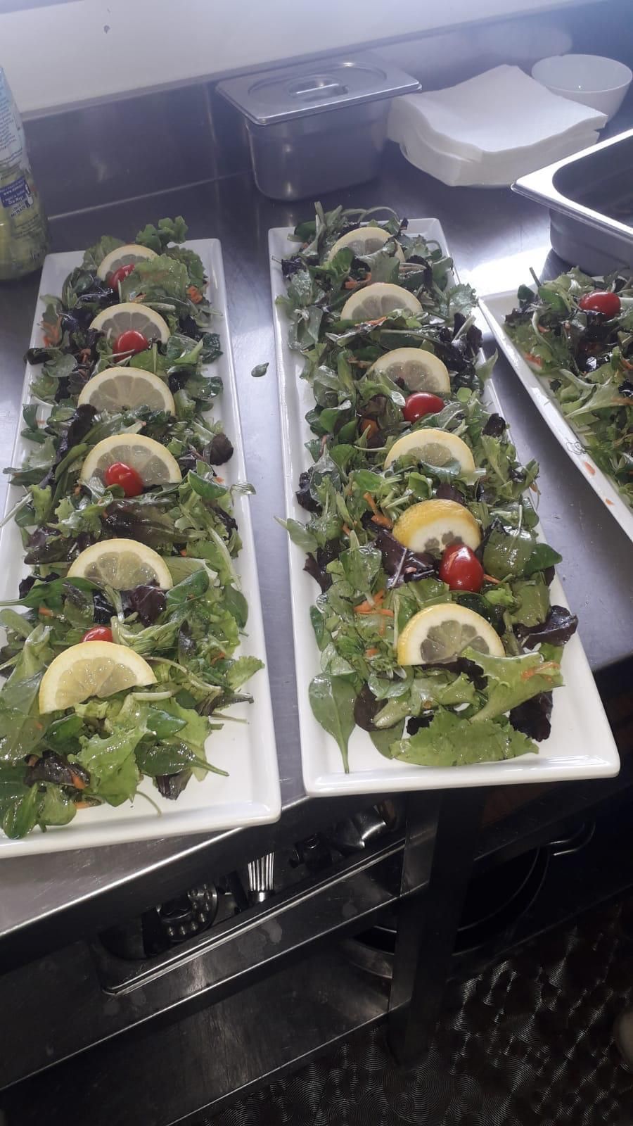 Due vassoi rettangolari di insalata guarniti con fette di limone e pomodori su un bancone.