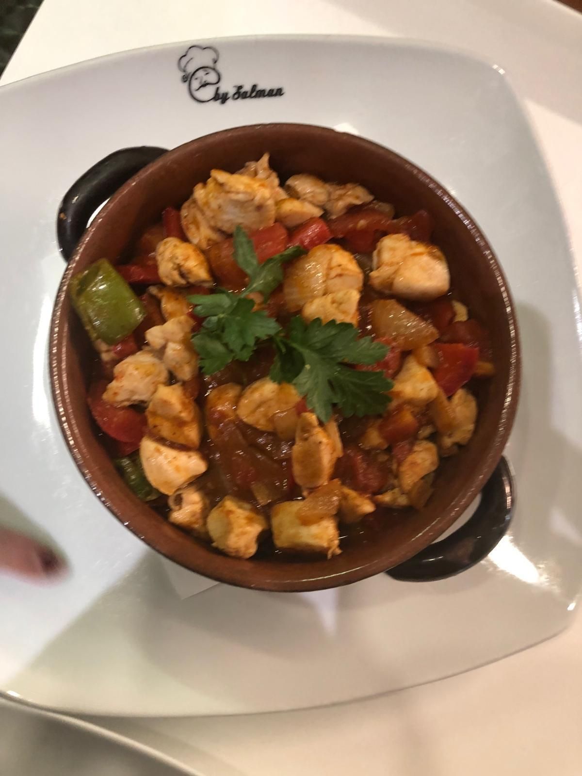 Stufato di pollo e verdure in una piccola ciotola marrone, guarnito con prezzemolo su un piatto bianco.