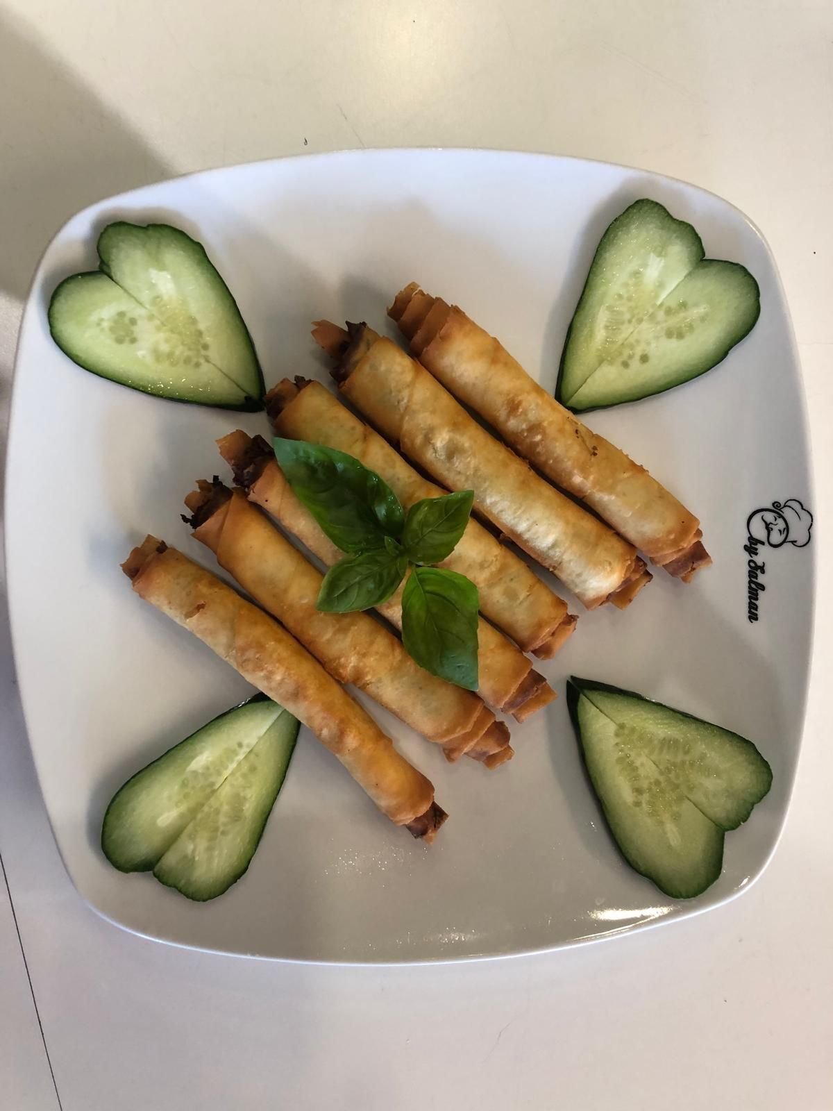 Piatto di rotoli di pasta sfoglia dorati con cuori di cetriolo e un rametto di basilico.
