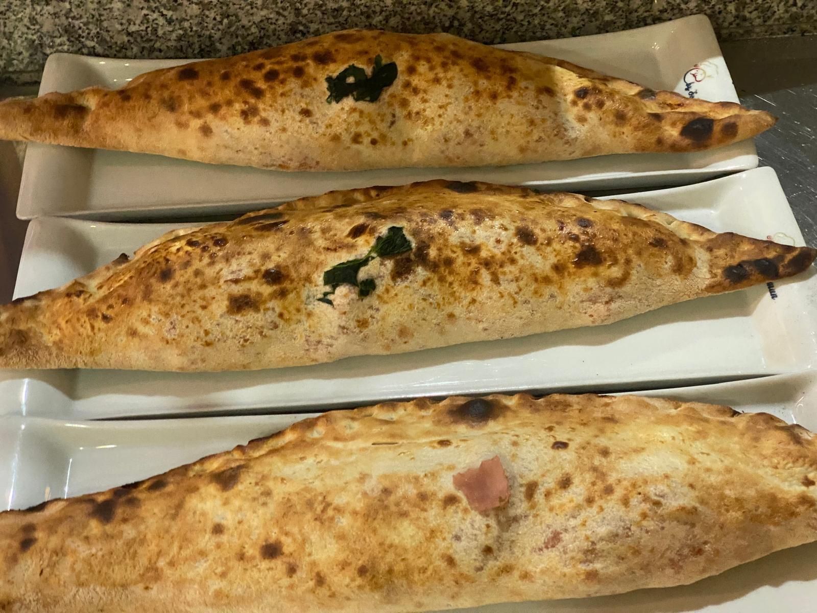 Tre calzoni cotti al forno su piatti rettangolari bianchi. La crosta è dorata con macchie scure.