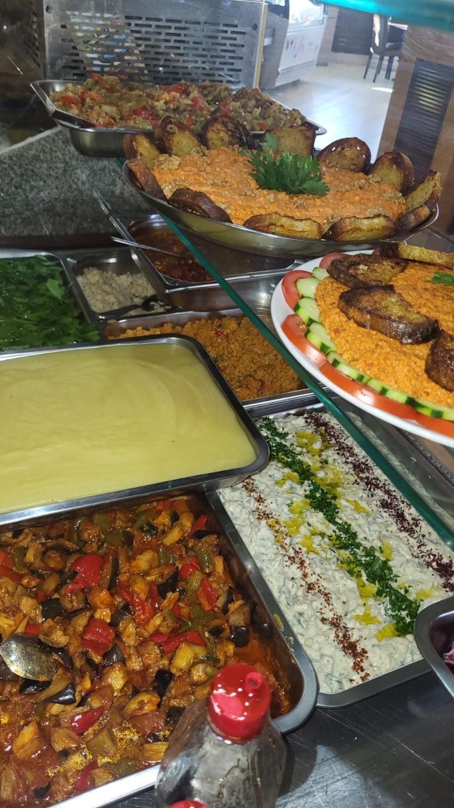 Esposizione di vari cibi preparati, tra cui riso, stufati e verdure, in un ambiente da ristorante.