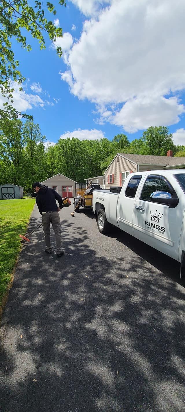 A man standing next to a white pickup truck with a trailer on a driveway. Blue sky overhead.