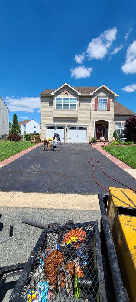 A house with a new black asphalt driveway being paved on a sunny day.