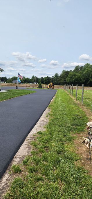 A new black asphalt path next to a grassy area with a fence, blue sky.