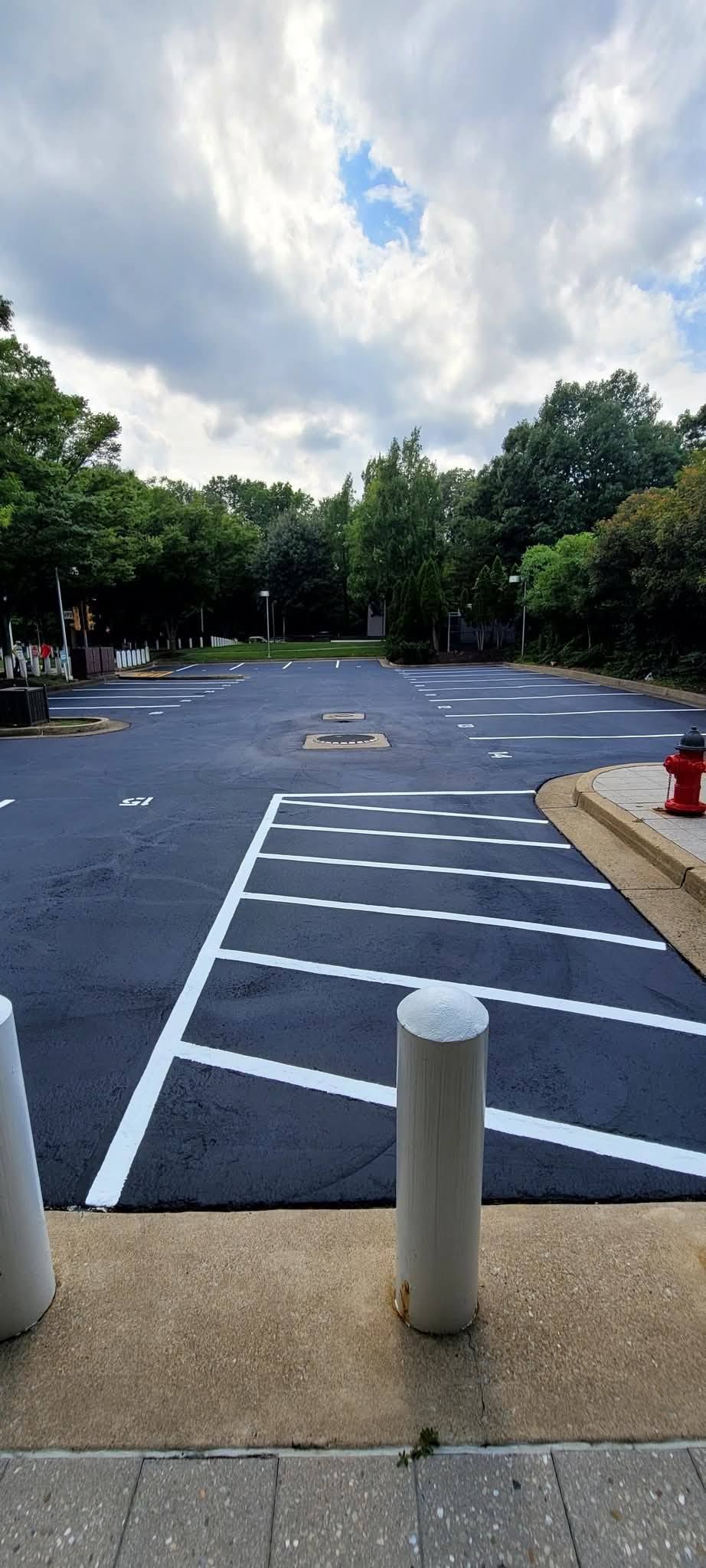 Newly paved parking lot with white parking lines, a fire hydrant, and trees. Overcast sky.