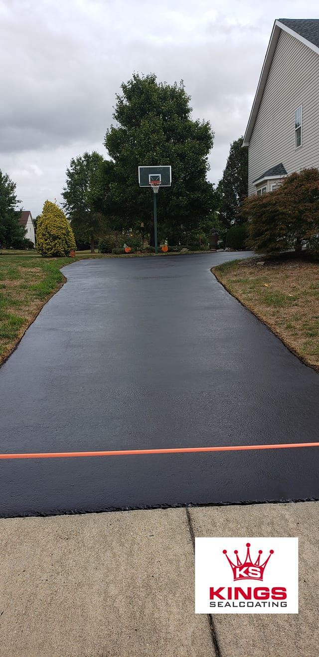Black asphalt driveway with basketball hoop and house in the background. Kings Solutions logo.