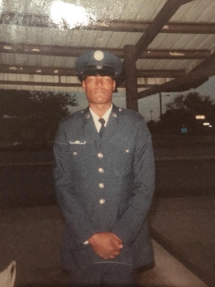A man in a military uniform stands with his hands folded