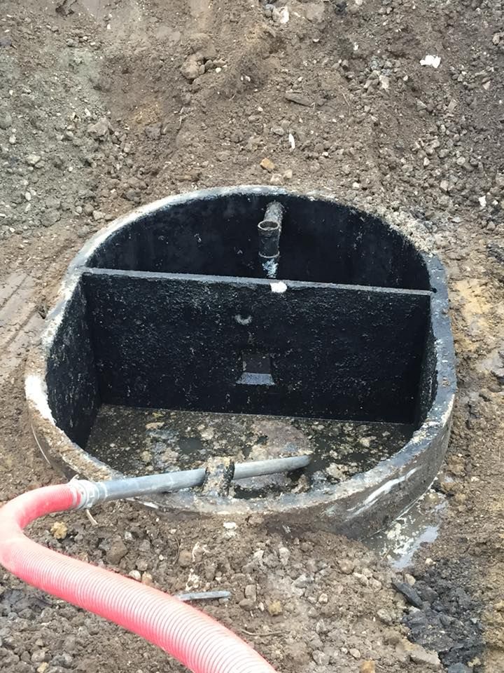 Open septic tank with water, a dividing wall, and a red hose extending from it, set in dirt.
