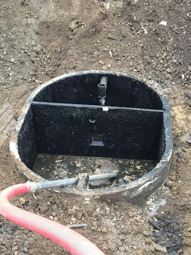 Open septic tank with water, a dividing wall, and a red hose extending from it, set in dirt.