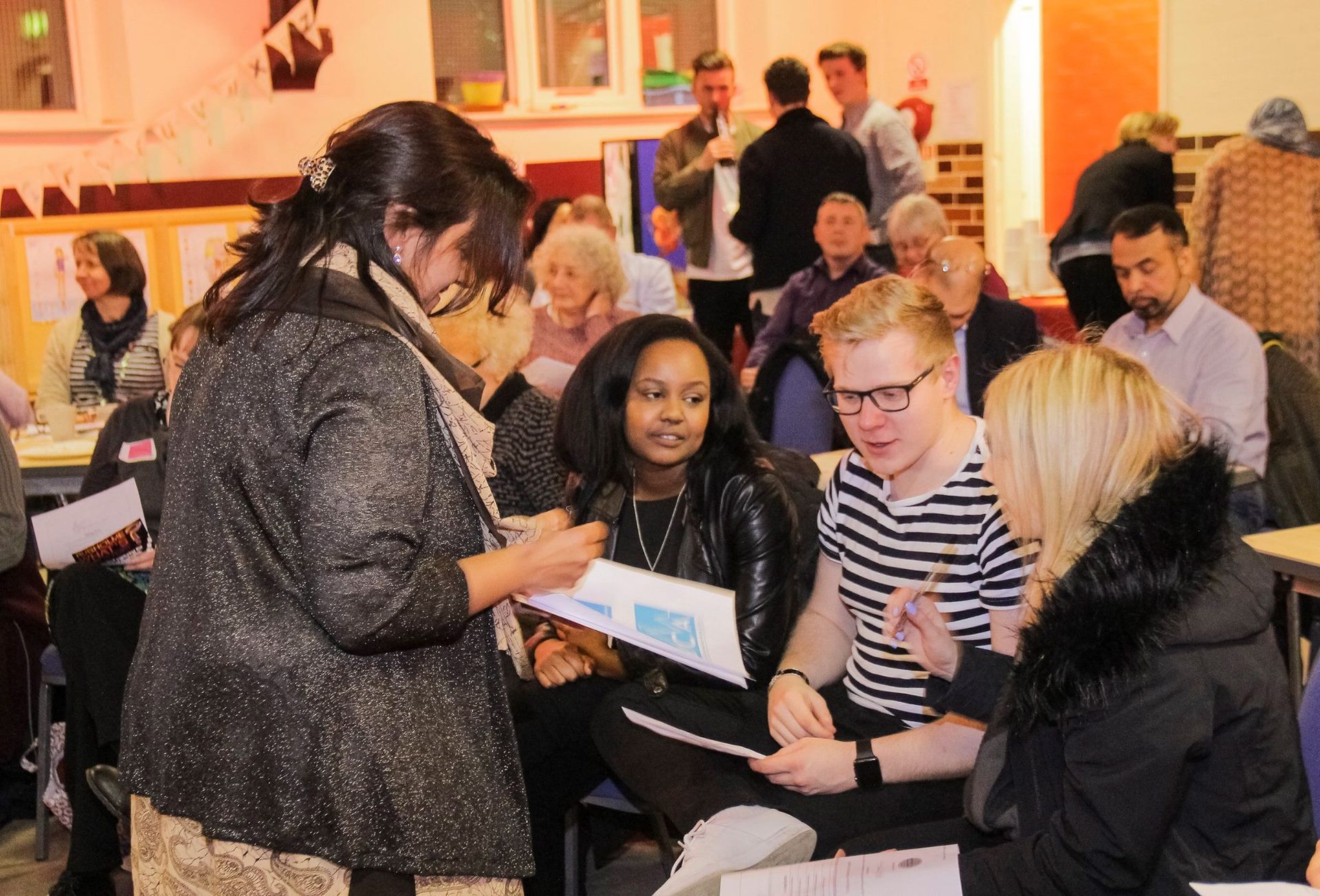 A woman is talking to a group of people sitting around a table.