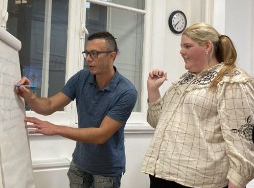 A man and a woman are standing next to each other in front of a whiteboard.