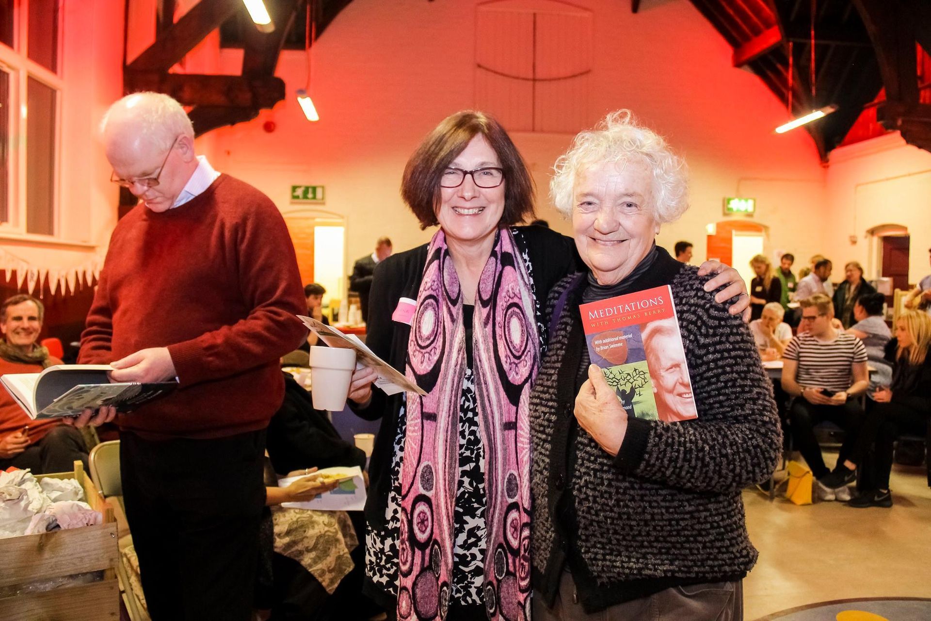 Two women are standing next to each other in a room holding books.